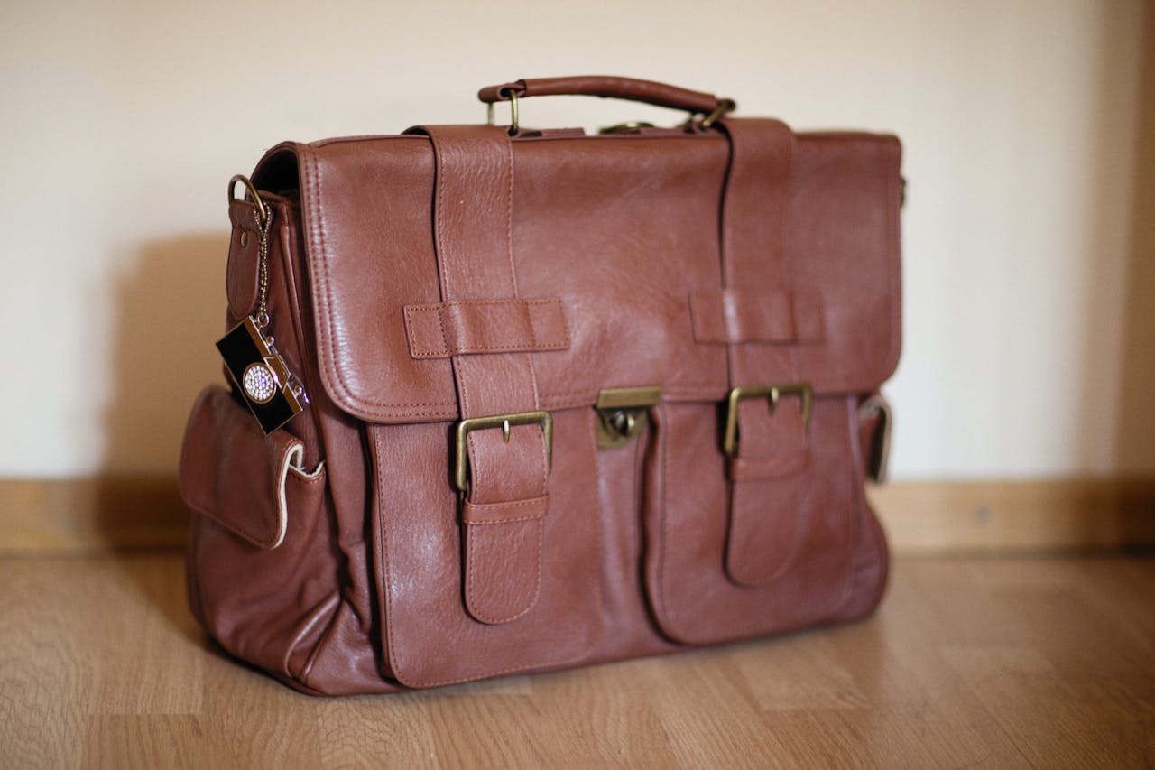 Close-up of an elegant brown leather briefcase with brass buckles on a wooden floor.