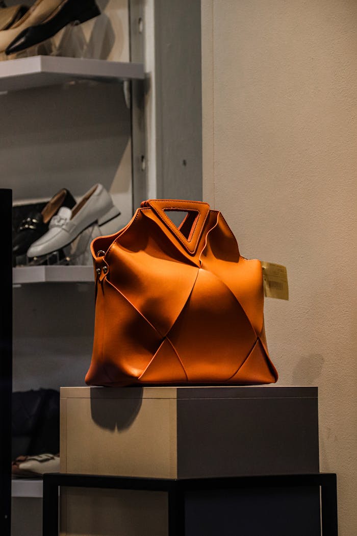 A striking orange designer handbag showcased elegantly on a stand in a retail store.